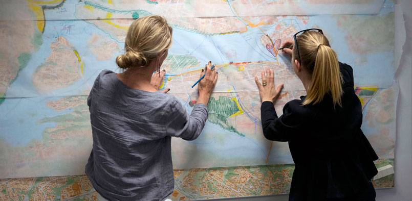 Två kvinnor vid vägg med stora kartor